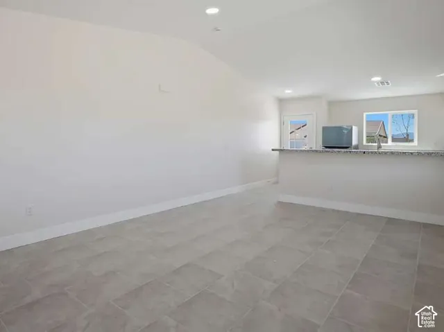Open-concept living area featuring neutral-toned tile flooring, recessed lighting, and a kitchen island with a speckled countertop