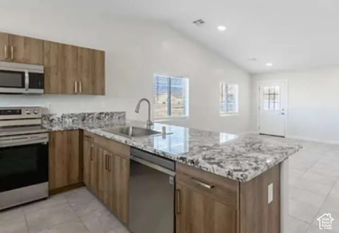 Kitchen with wood-finish cabinetry, stainless steel appliances, and a central island featuring a stone countertop with an undermount sink