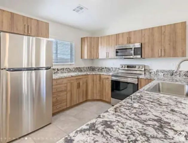 Stainless steel appliances, wood-finish cabinetry, stone countertops, and a stainless steel sink with a high-arc faucet