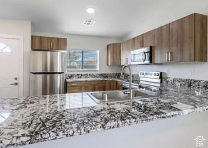 Kitchen featuring extensive countertops, a stainless steel sink with a gooseneck faucet, integrated stainless steel appliances, and wood-finish cabinetry
