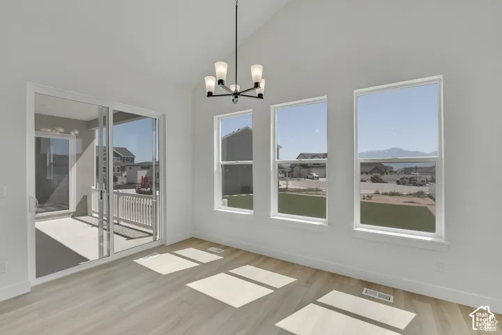 Vaulted ceiling with a contemporary chandelier, multiple windows, wood-finish flooring, and a sliding glass door to a covered patio