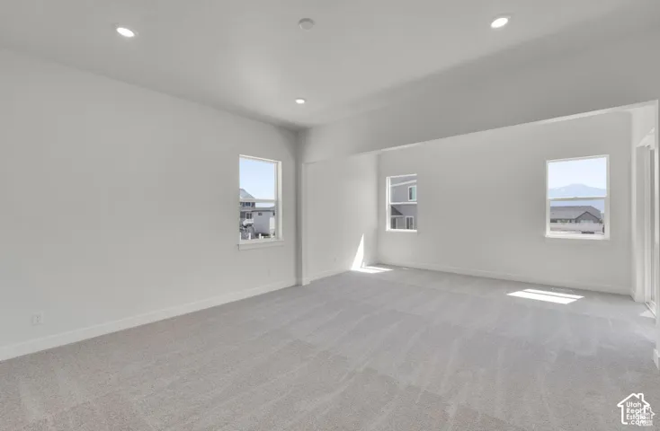Spacious room featuring light-colored carpeting, multiple windows, recessed lighting, and crisp white walls