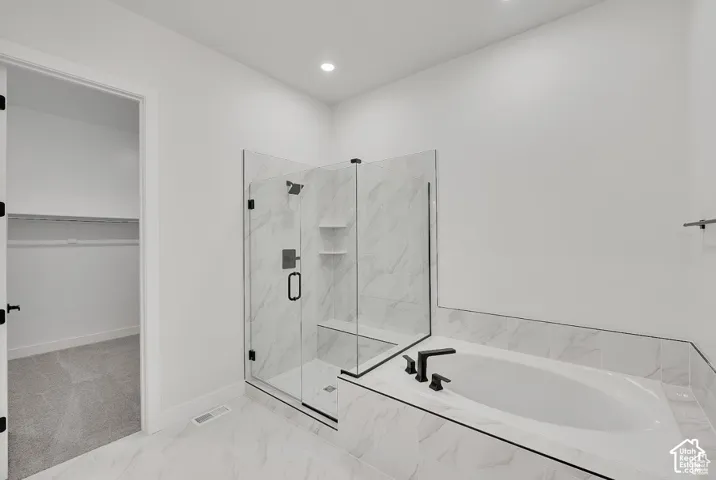 White soaking tub with black fixtures, walk-in shower with clear glass enclosure, and white tile flooring