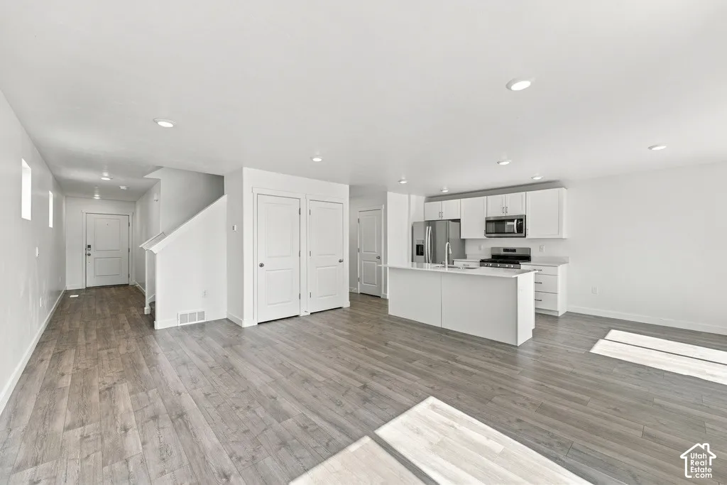 Open-concept living space with wood-finish flooring, recessed lighting, a modern kitchen island, stainless steel appliances, and white cabinetry