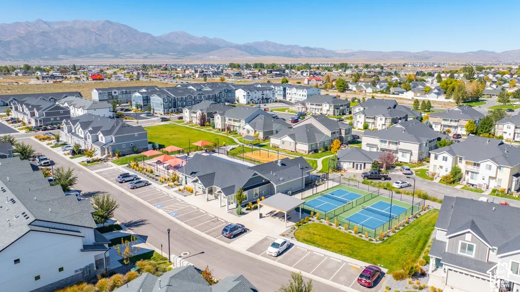 Community featuring residential buildings, tennis courts, open green spaces, and mountain backdrop
