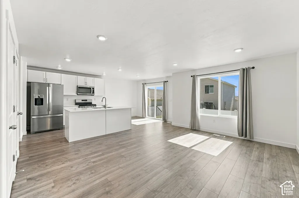 Open-concept living area with wood-finish flooring, recessed lighting, white cabinetry, and stainless steel appliances