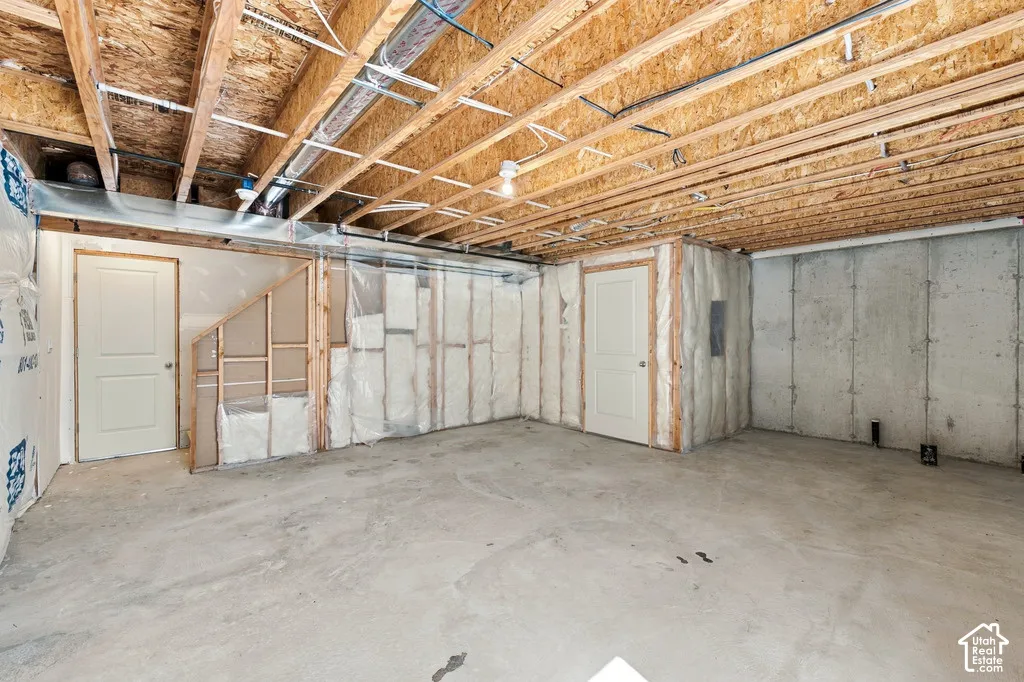 Unfinished basement with exposed ceiling joists, concrete flooring, and two paneled doors