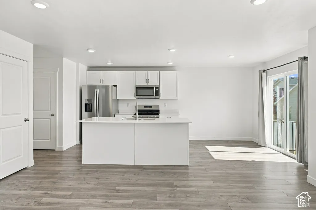 Modern kitchen featuring white cabinetry, stainless steel appliances, a center island with sink, and wood-finish flooring