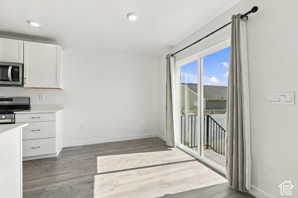 White shaker cabinetry, stainless steel appliances, wood-finish flooring, recessed lighting, and a sliding glass door to an exterior balcony with black railings