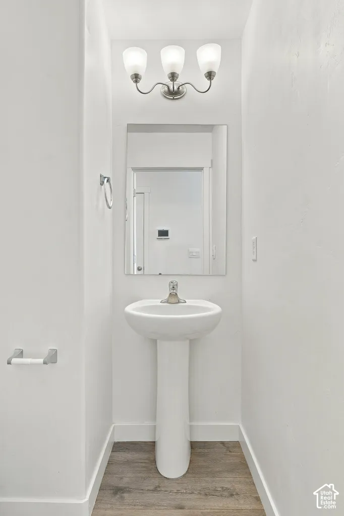 Pedestal sink, wall-mounted rectangular mirror, three-light vanity fixture, wood-finish flooring, and a towel ring