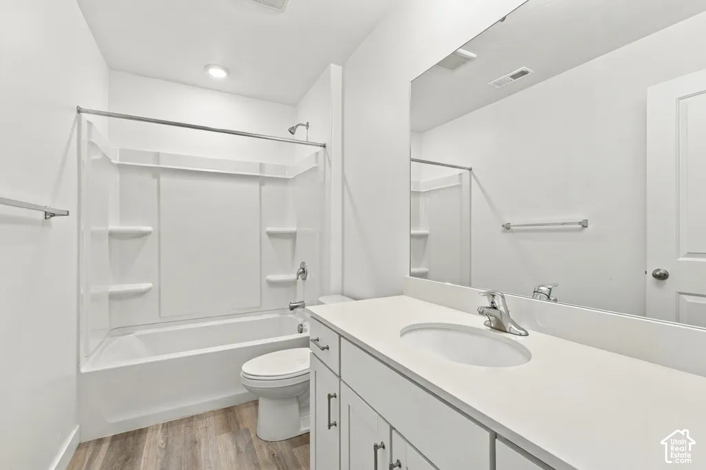 Wood-finish flooring, white vanity with integrated sink, chrome hardware, full-width mirror, and a white tub with shower
