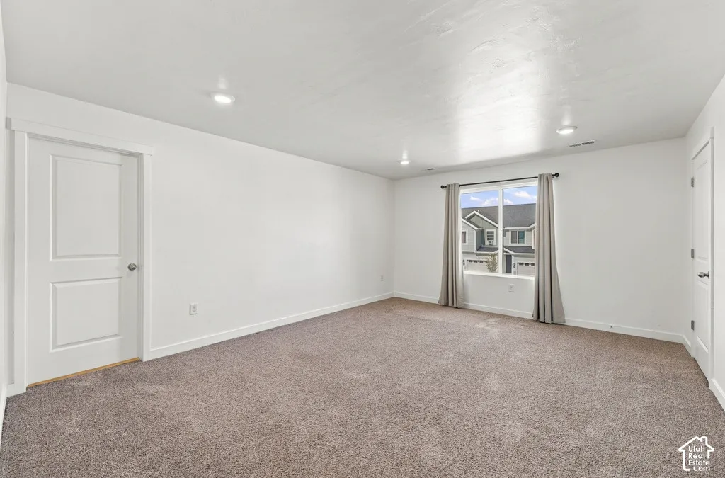 Spacious room with plush carpeting, recessed lighting, white walls, and a large window