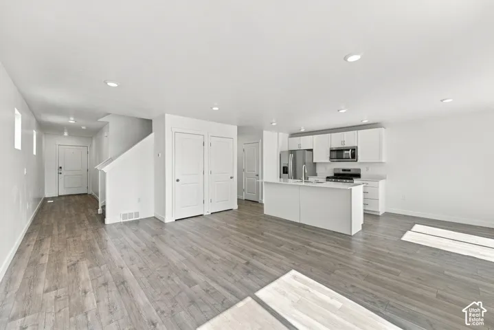 Open-concept living space with wood-finish flooring, recessed lighting, a modern kitchen island, stainless steel appliances, and white cabinetry