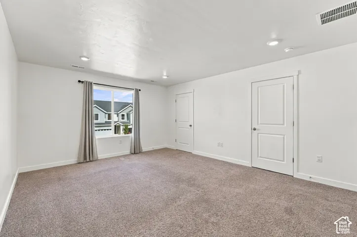 Spacious room featuring neutral carpet, recessed lighting, and a large window with white trim