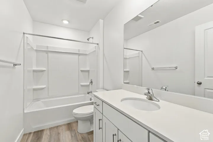 Wood-finish flooring, white vanity with integrated sink, chrome hardware, full-width mirror, and a white tub with shower