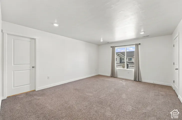 Spacious room with plush carpeting, recessed lighting, white walls, and a large window