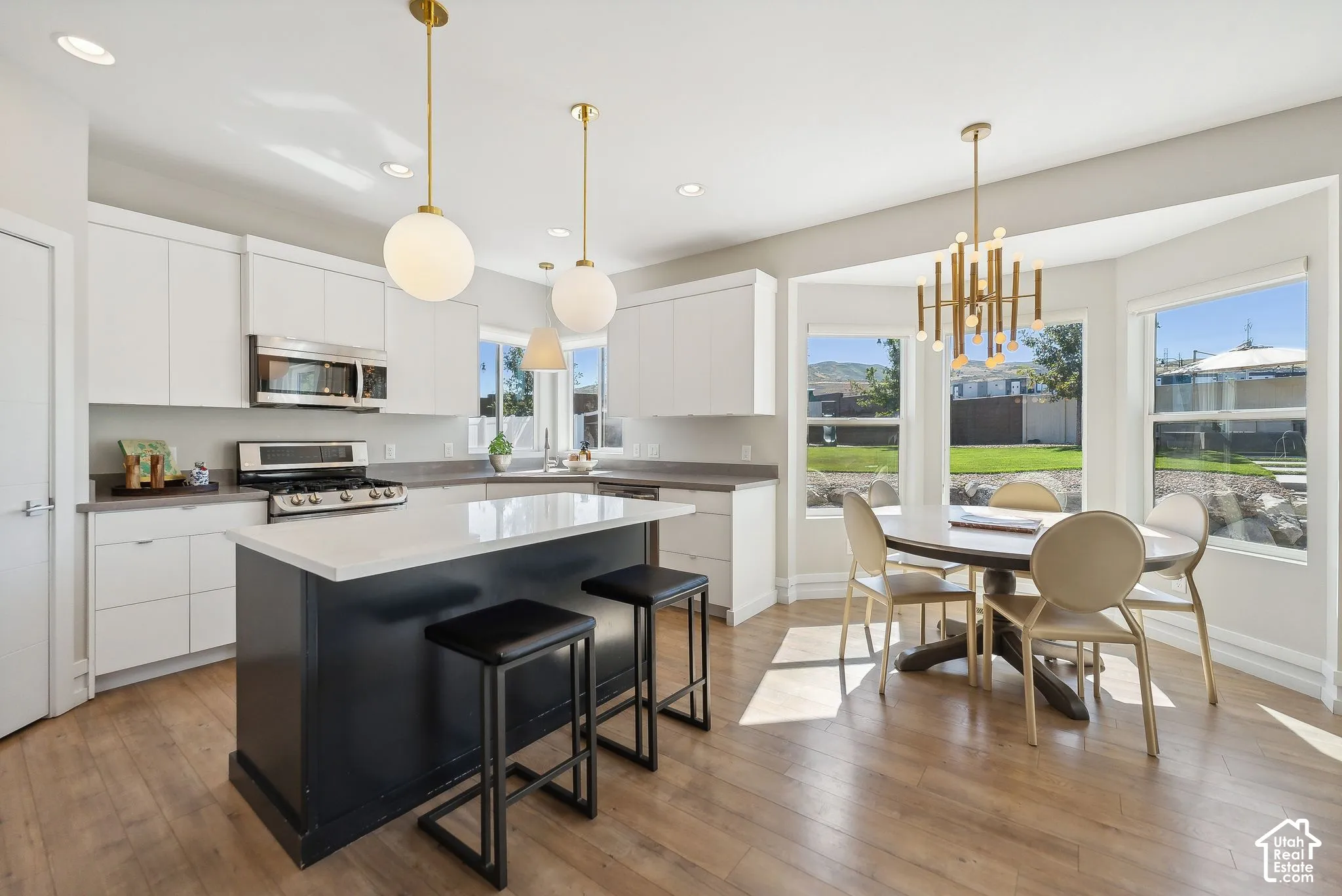Modern kitchen featuring white cabinetry, stainless steel appliances, a dark-toned island with a light-toned countertop, and wood-finish flooring