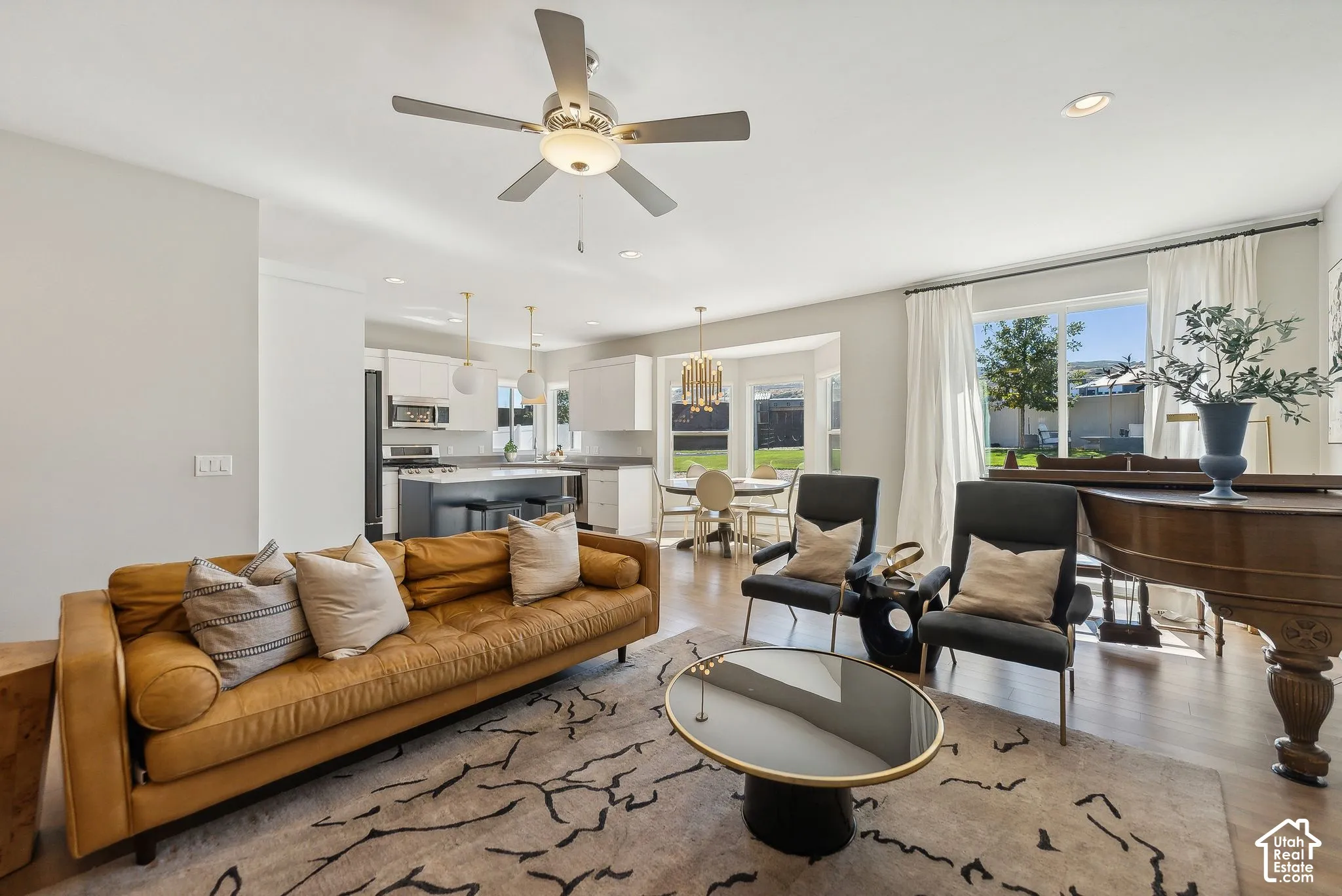 Open-concept living area with wood-finish flooring, a ceiling fan, recessed lighting, and large windows with drapery