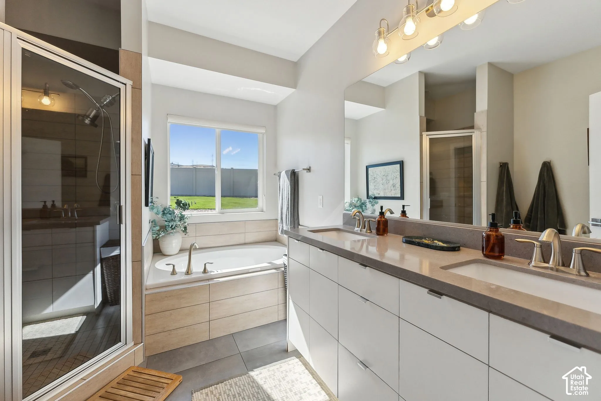 Dual vanity with undermount sinks, a built-in soaking tub, a separate glass-enclosed shower, and a large window