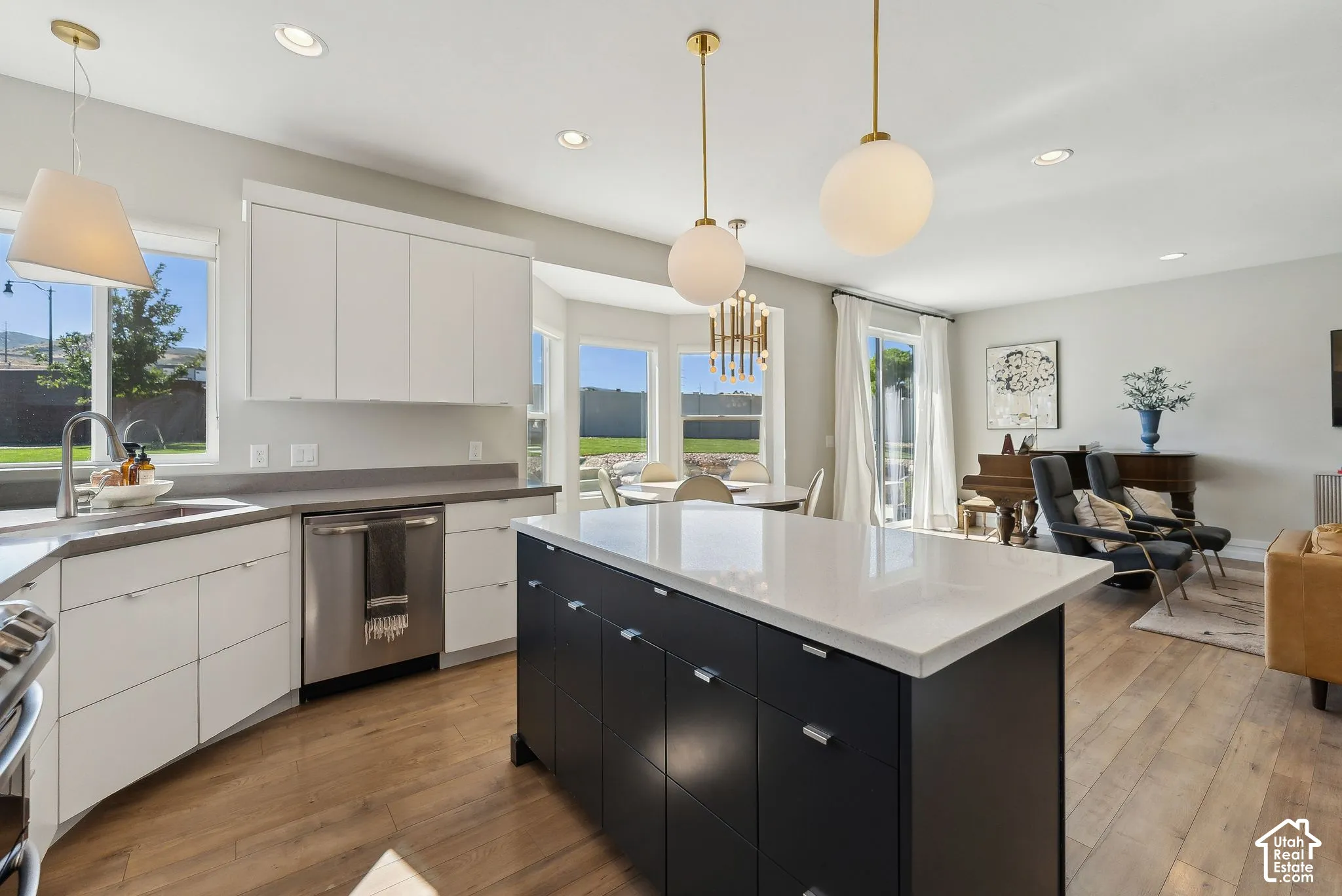 White flat-panel cabinetry, stainless steel appliances, wood-finish flooring, central island with light-colored countertop, and recessed lighting