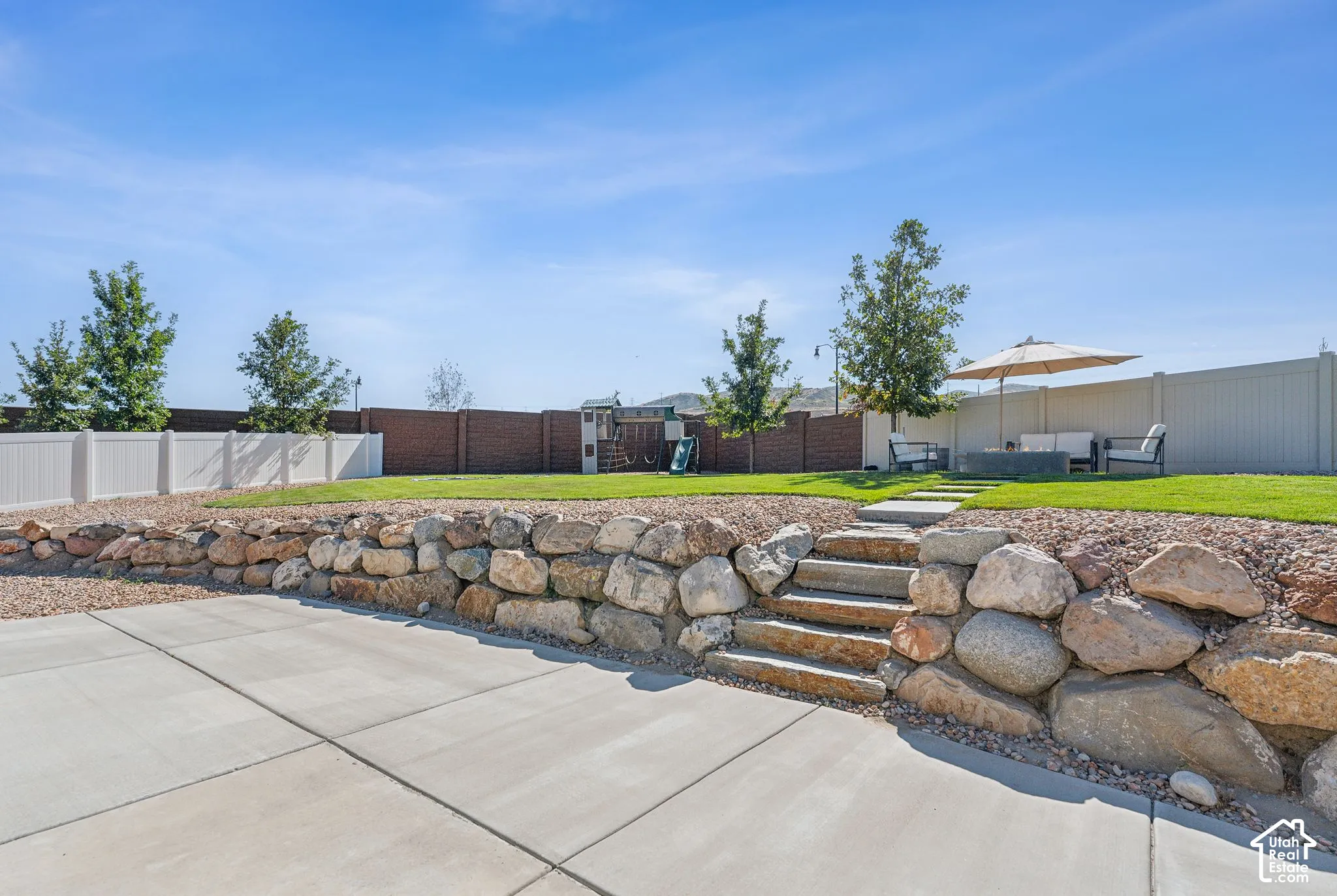 Expansive concrete patio with a stone retaining wall and integrated stone steps