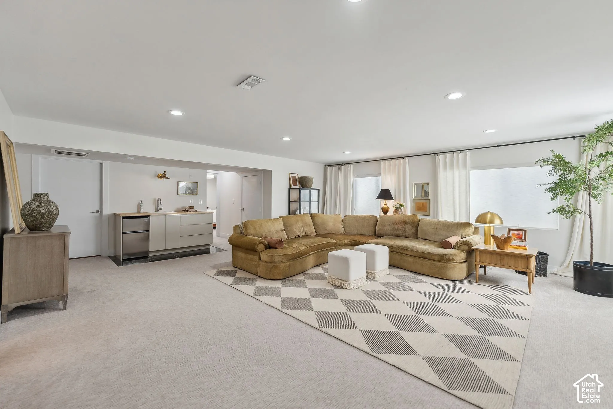Recessed lighting illuminating a spacious room with light-toned carpeting and a built-in wet bar featuring a stainless steel under-counter appliance
