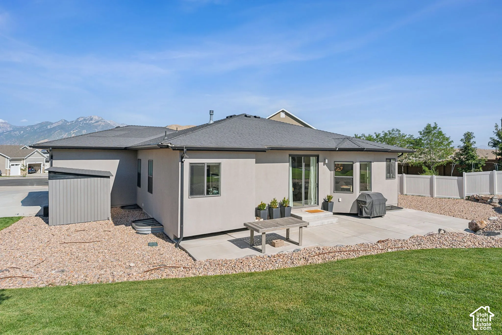 Stucco exterior with a dark shingle roof, featuring sliding glass doors and multiple windows