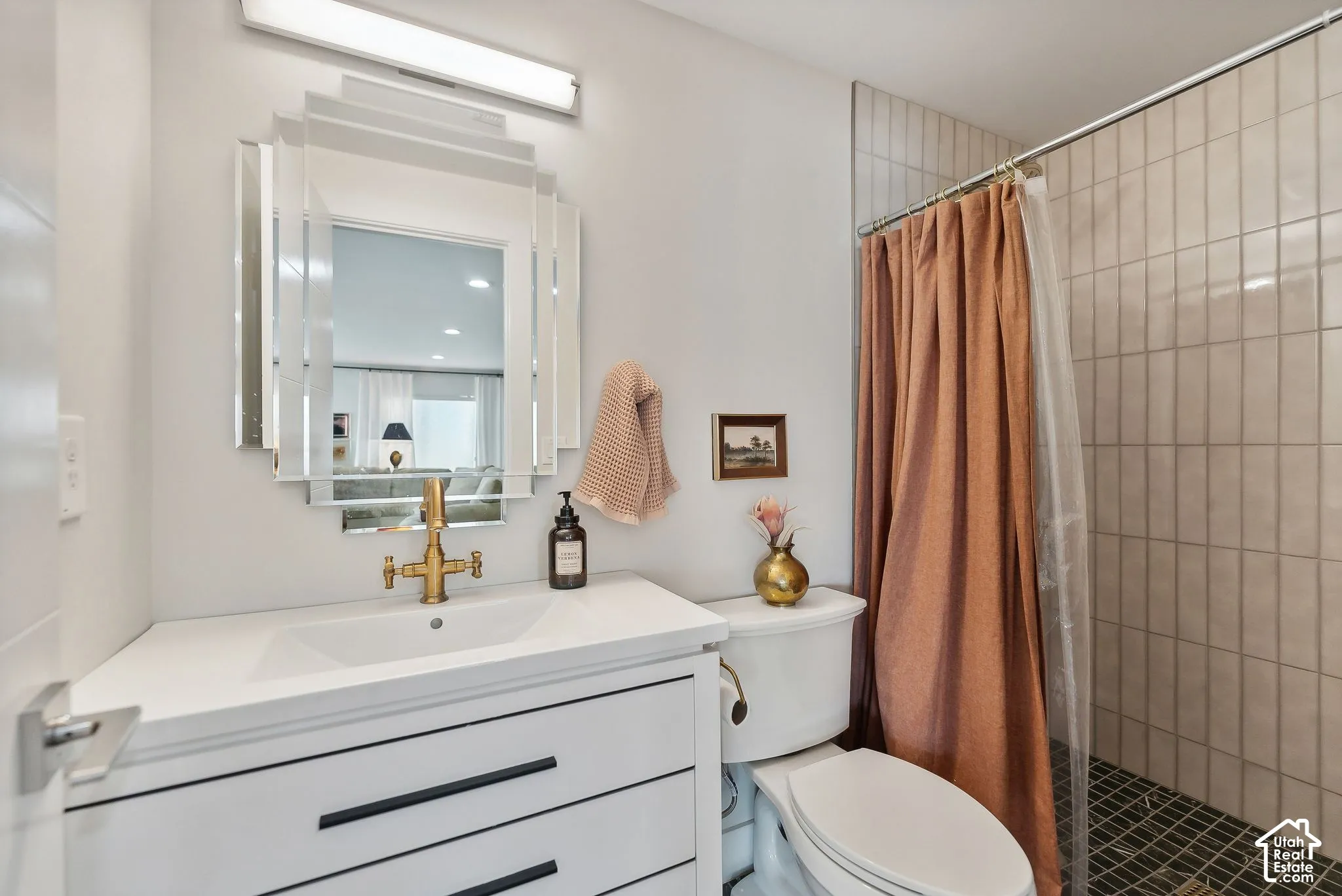 White vanity with black hardware, integrated sink, and brass-finish faucet