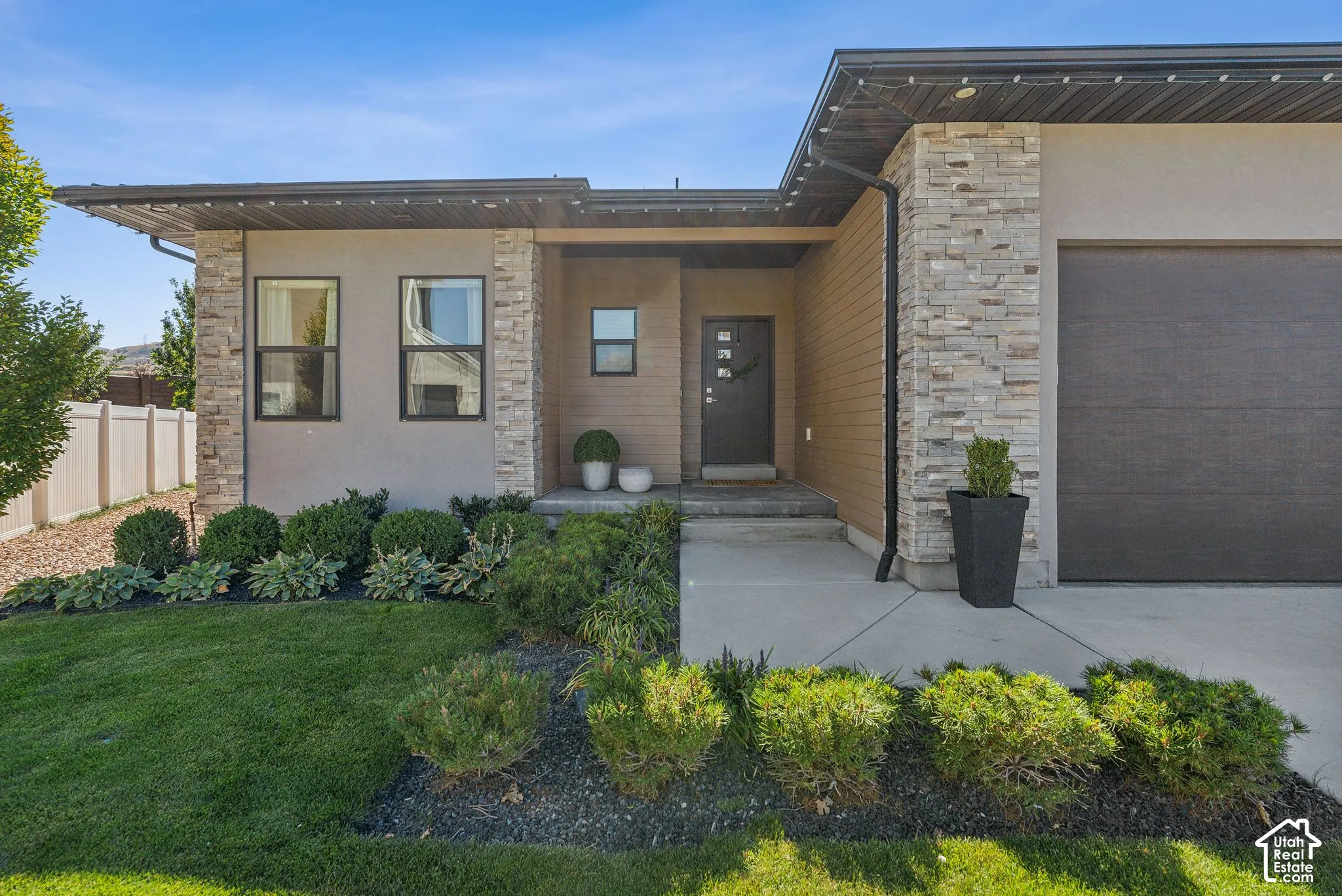 Contemporary exterior featuring stone veneer accents, stucco siding, a covered entry, and a dark-finish garage door