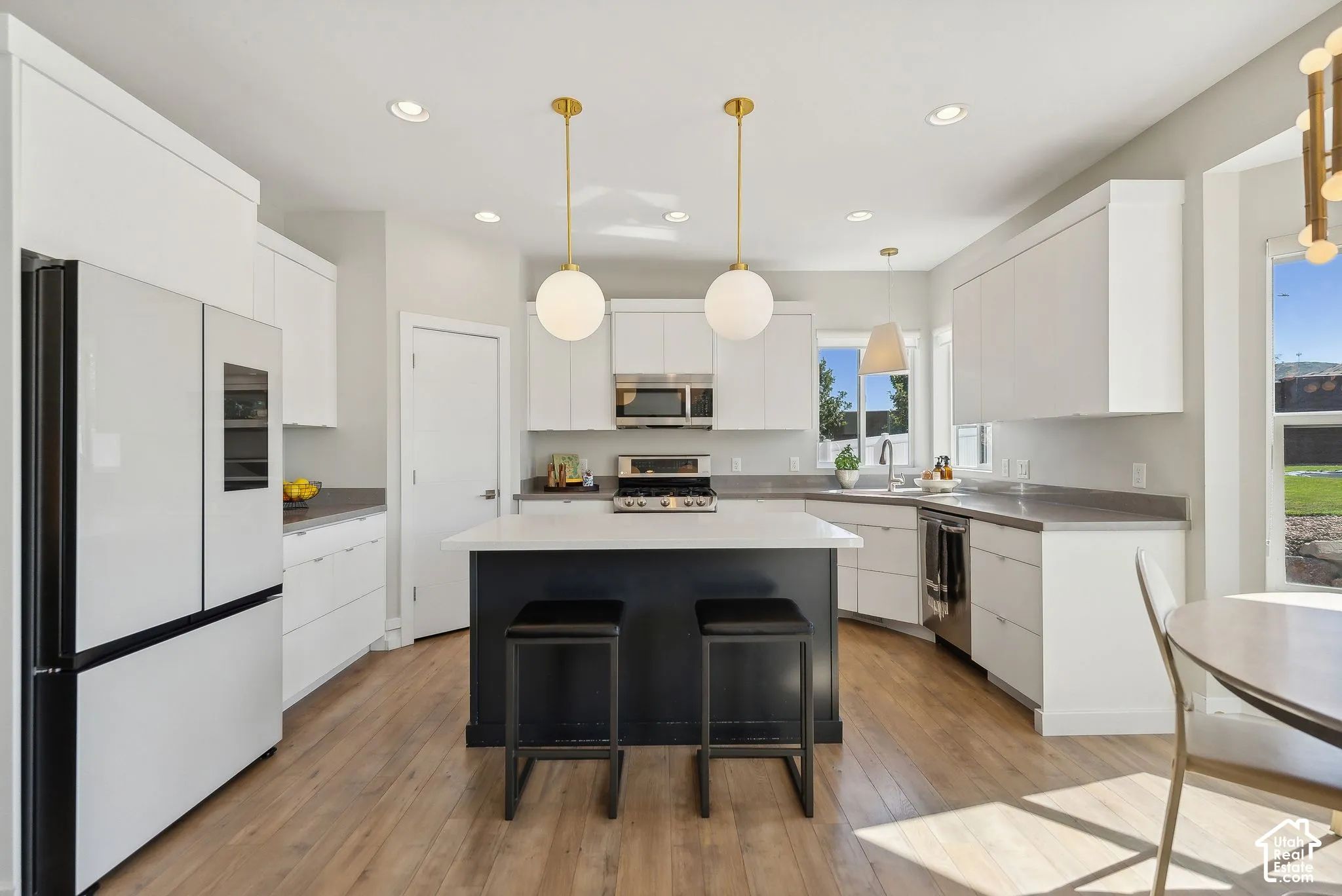 Wood-finish flooring throughout the kitchen with white cabinetry and a contrasting dark island