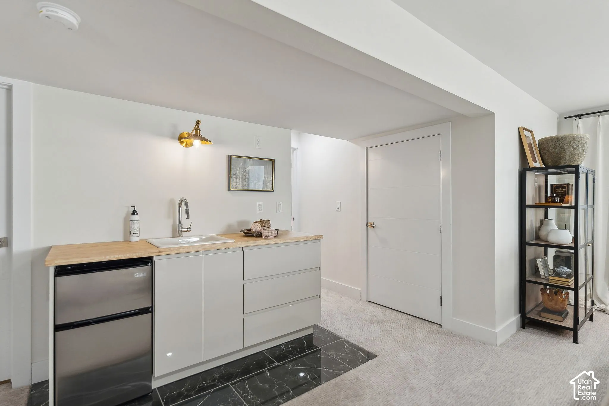 Compact kitchenette with light wood-finish countertop, white cabinetry, integrated sink, and stainless steel undercounter refrigerator