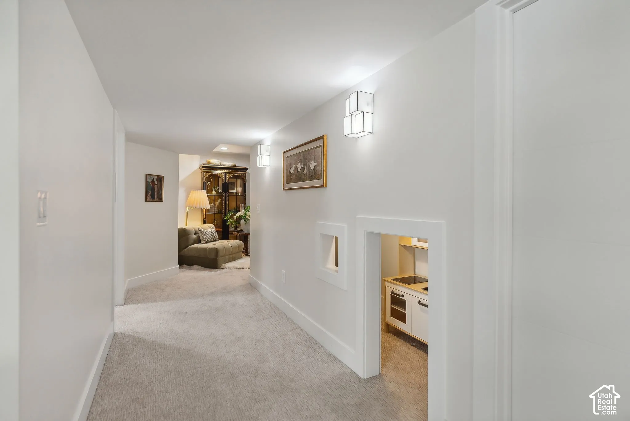 Carpeted hallway with white walls, recessed ceiling lighting, and wall-mounted sconces
