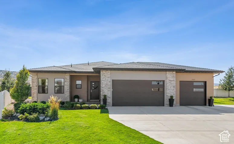 Contemporary stucco exterior with stone veneer accents, a dark-toned roof, and an attached two-car garage