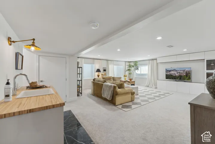 Spacious recreation area featuring recessed lighting, a built-in media center with storage, a wet bar with a wood-finish countertop and basin sink, and ample natural light