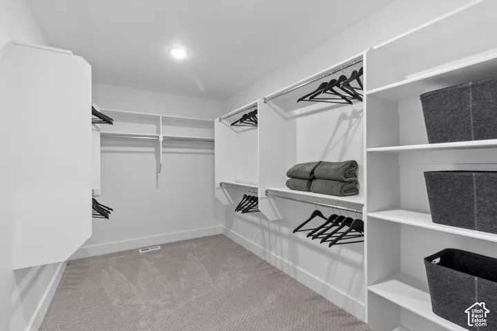 Recessed ceiling lighting illuminates a spacious closet featuring extensive built-in shelving, multiple hanging rods, and light-toned carpeting