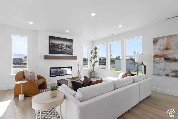 Recessed lighting, wood-finish flooring, a linear fireplace with a shiplap accent wall, and multiple windows