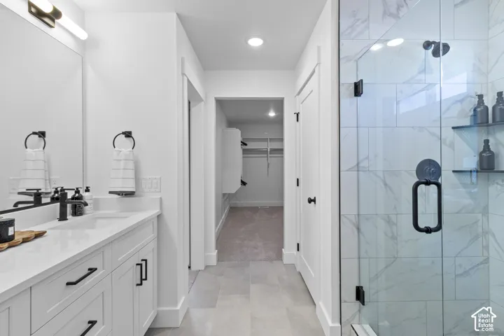 Bathroom featuring a vanity with an integrated sink, white cabinetry, matte black hardware, and a tiled walk-in shower with a glass enclosure