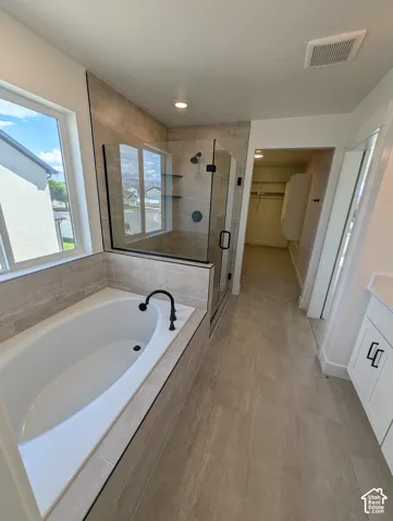 Soaking tub with matte black fixtures, glass-enclosed shower, wall-mounted shower system, and tile flooring