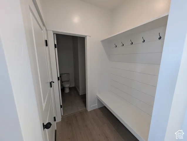 Built-in white shiplap bench with five black coat hooks and an overhead shelf