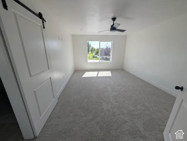 Spacious room featuring light-toned carpeting, a window providing natural illumination, and a ceiling fan