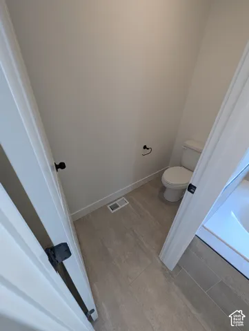 Powder room featuring a white toilet, light gray tile flooring, and white walls
