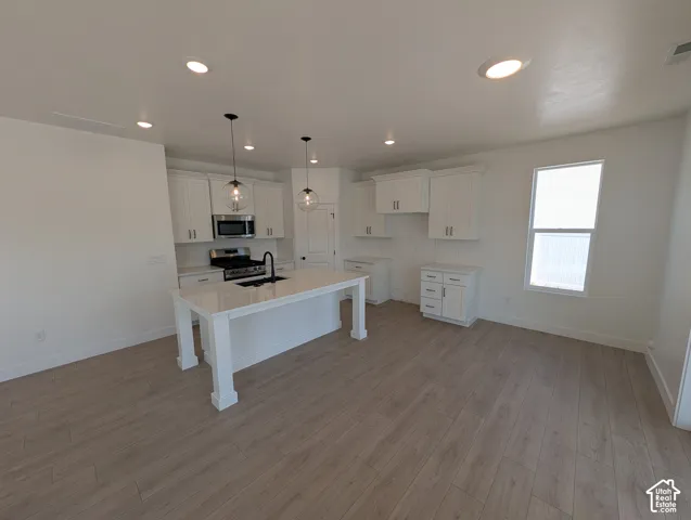 White shaker cabinetry, stainless steel appliances, wood-finish flooring, recessed lighting, and a kitchen island with pendant lighting