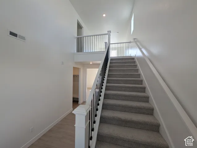 Carpeted staircase with black iron balusters, wood-finish flooring, and a second-story landing with matching balusters