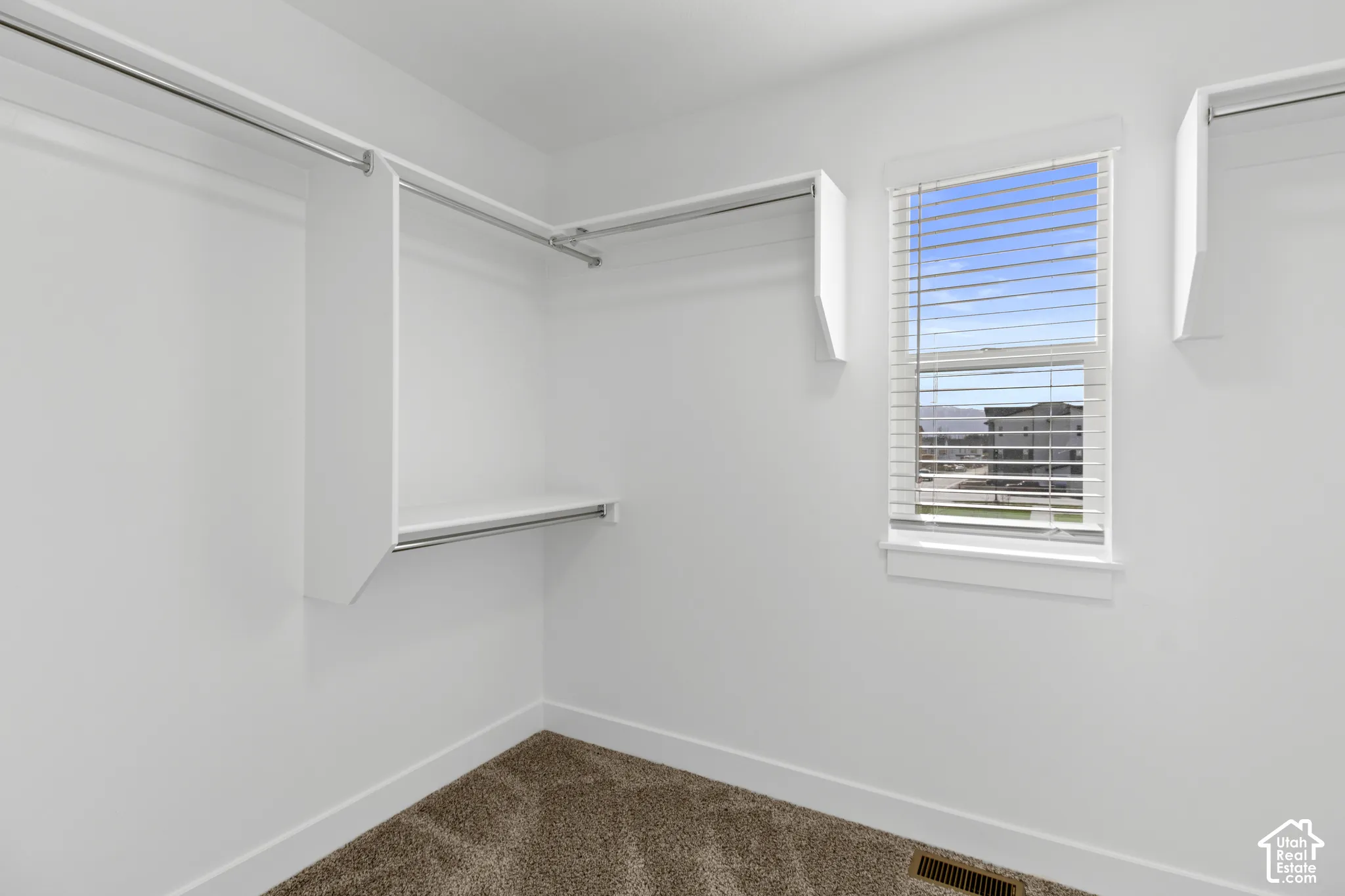 White walls with carpet flooring, featuring a window with horizontal blinds