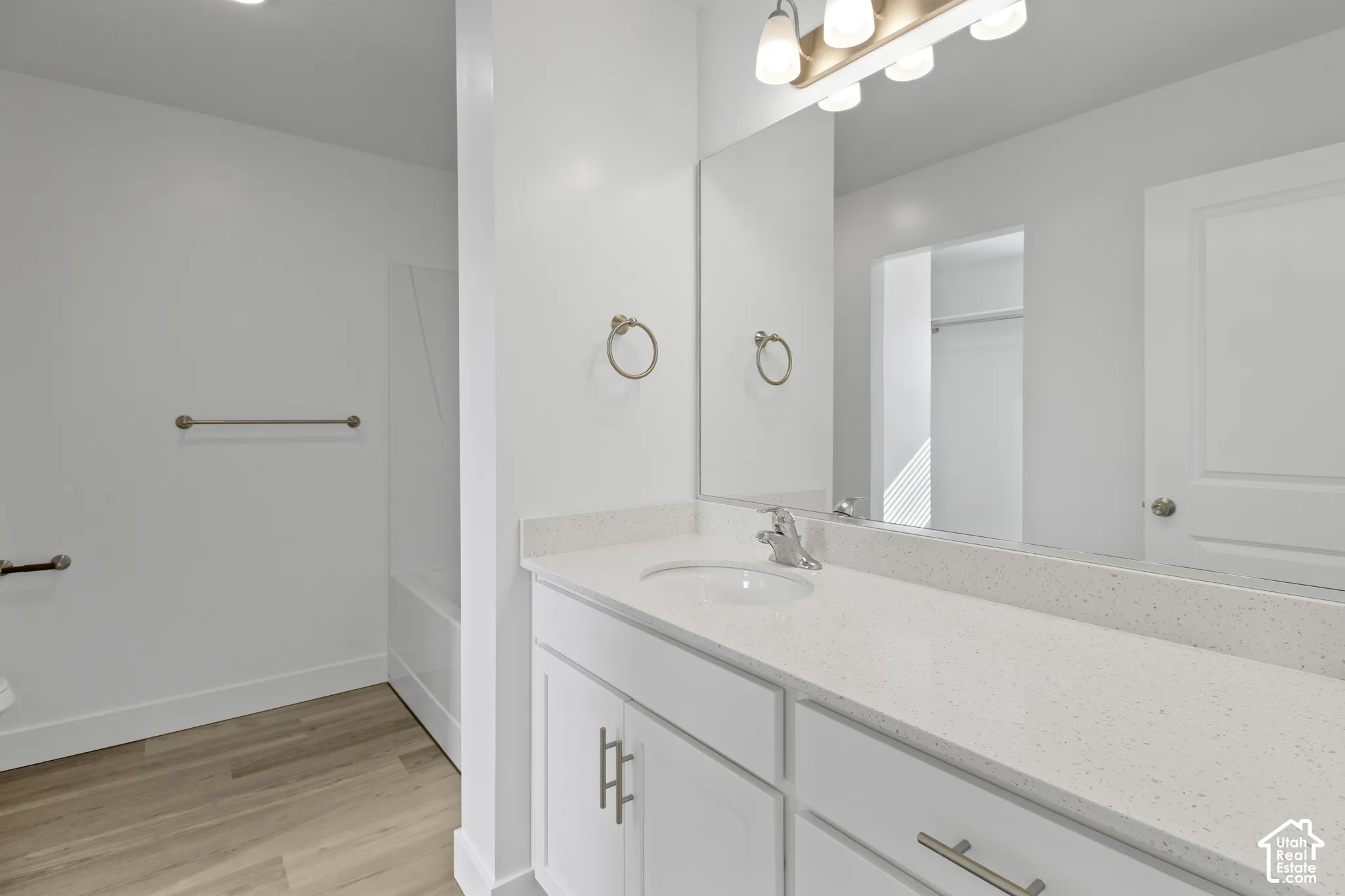 Bathroom featuring a white vanity with an integrated sink, broad wall mirror, and wood-finish flooring