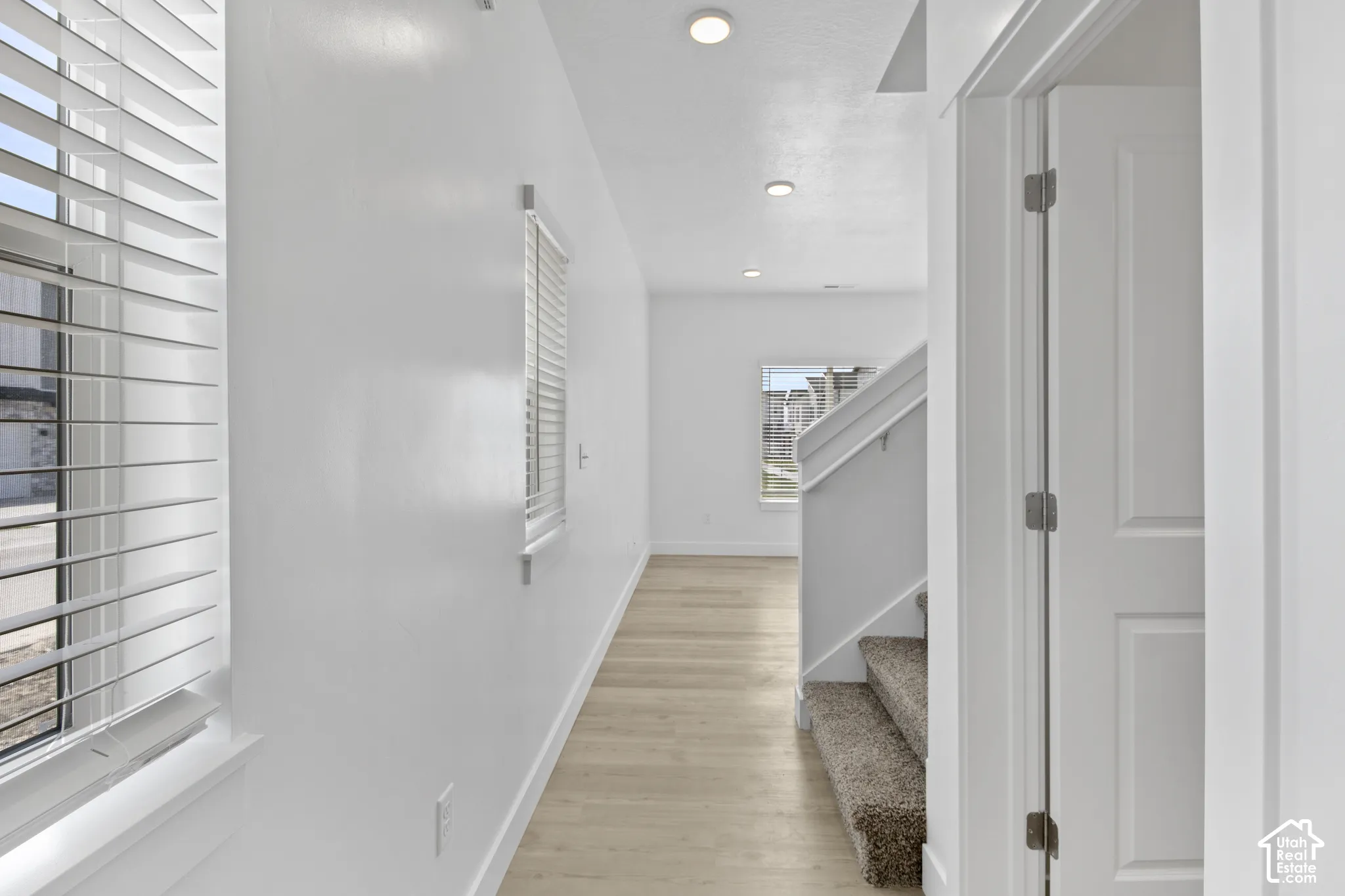 Recessed ceiling lighting, light wood-finish flooring, white horizontal blinds, and a carpeted staircase