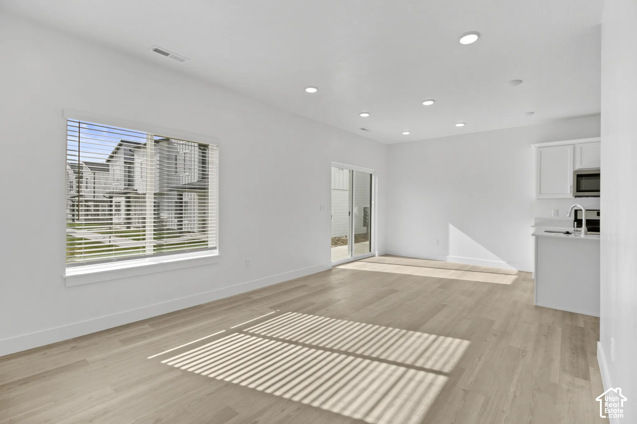 Spacious open-concept room featuring light wood-finish flooring, recessed lighting, and a sliding glass door