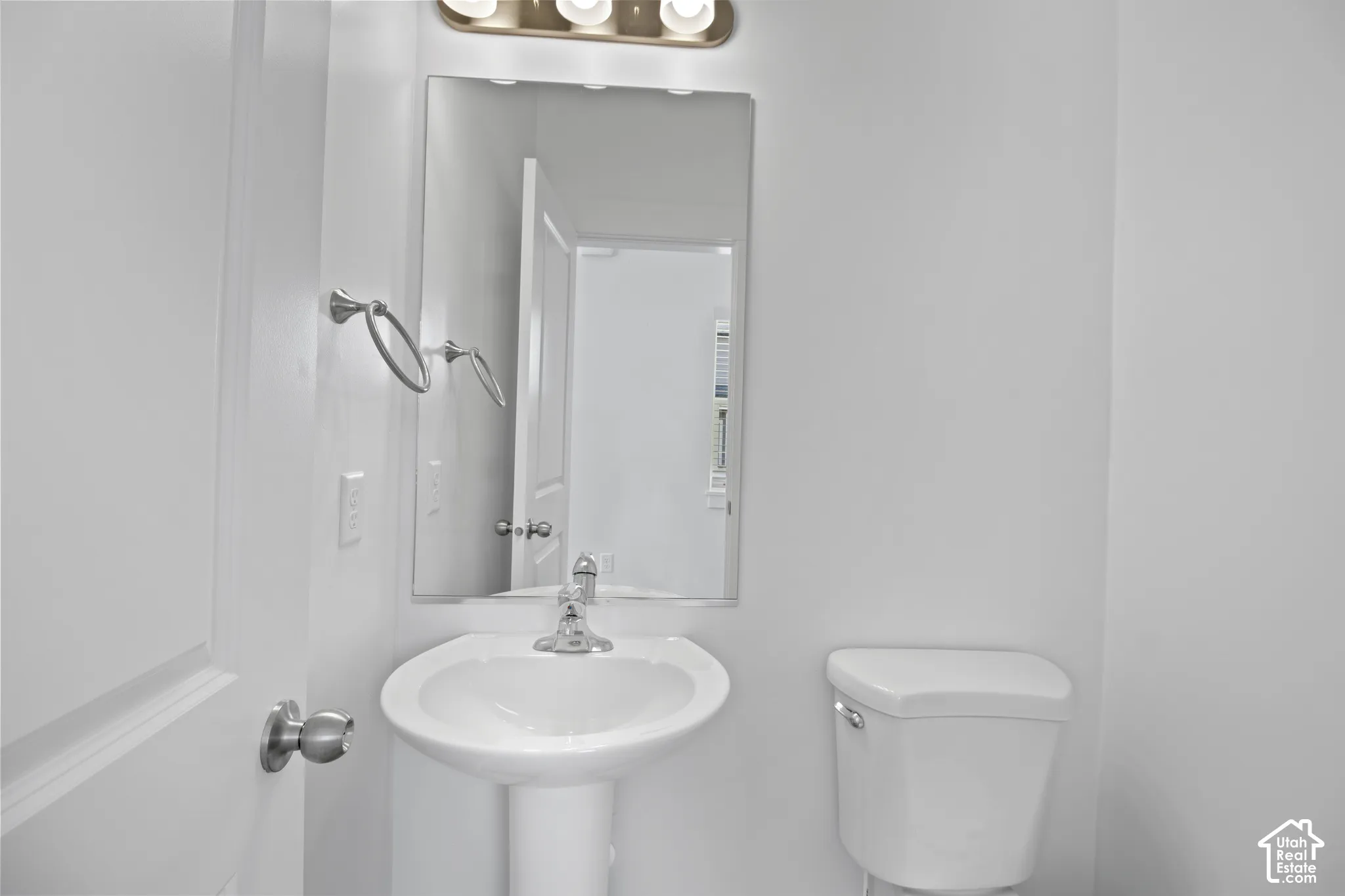 Pedestal sink with chrome faucet, wall-mounted mirror, and overhead vanity lighting