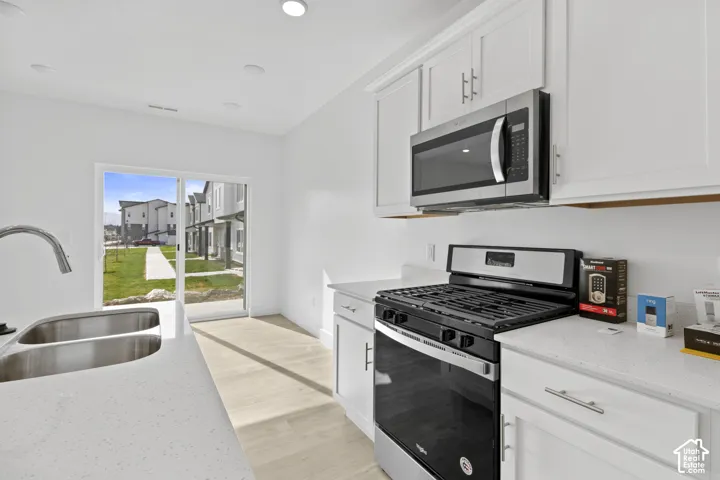 Modern kitchen featuring light-toned wood-finish flooring, white cabinetry with silver-tone hardware, and quartz countertops