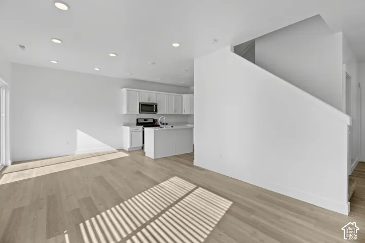 Open-concept living space with wood-finish flooring, recessed lighting, and a white kitchen featuring cabinetry, a microwave, and a stainless steel sink